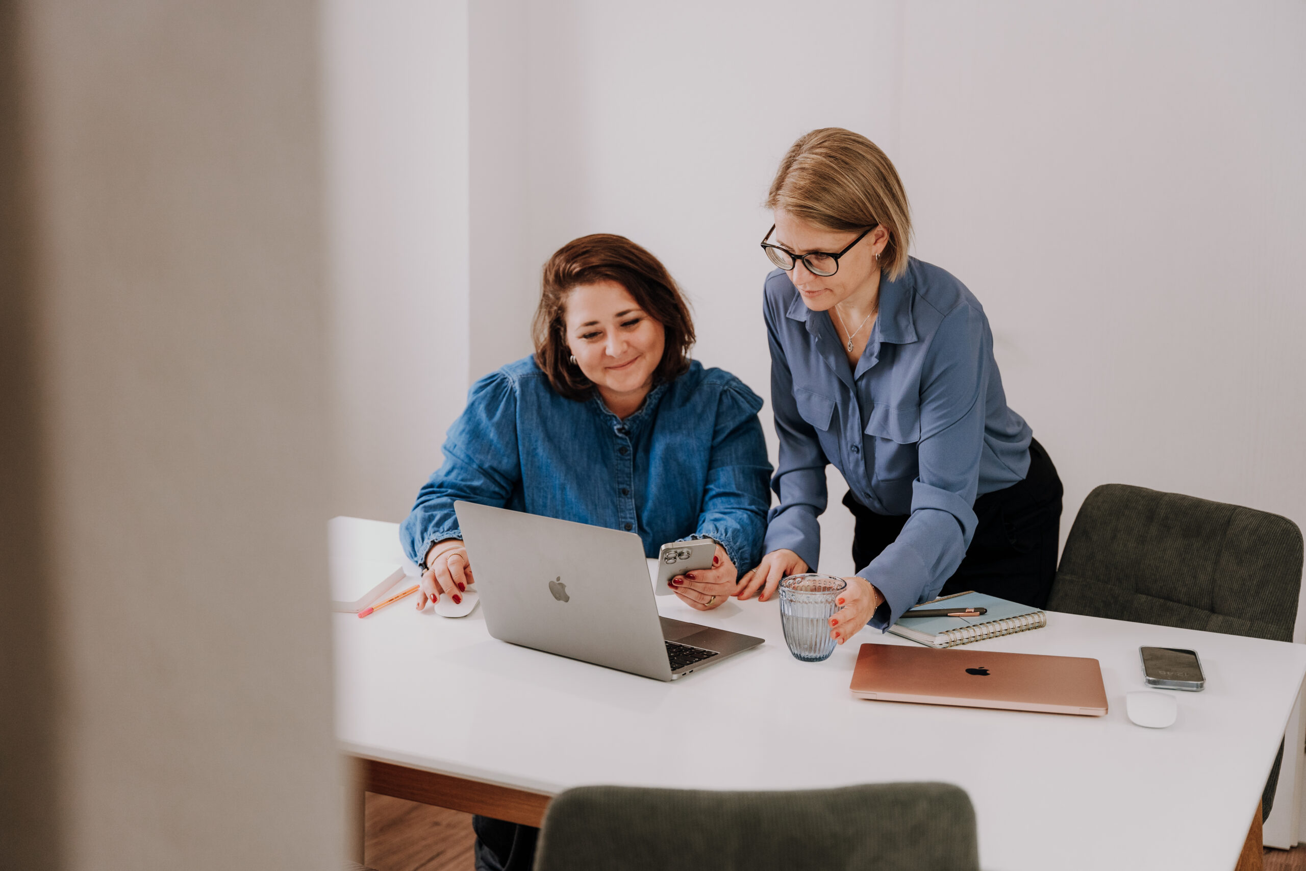 Zwei Frauen am Schreibtisch, eine sitzt, eine steht, beide schauen auf ein Laptop